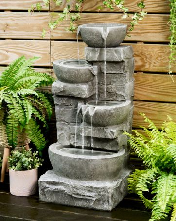 a stacked stone fountain sits in an outdoor garden