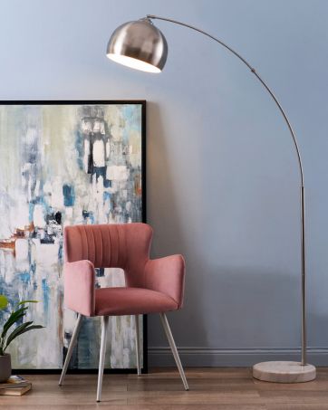 an arc floor lamp spotlights a living room accent chair in an artsy room
